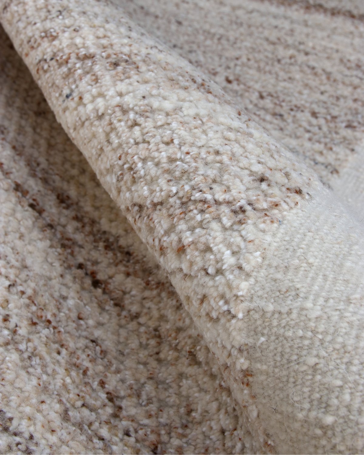 Close-up of Akira hand-knotted wool rug in Dune, showing the pile texture and flecked ivory and brown tones with folded edge
