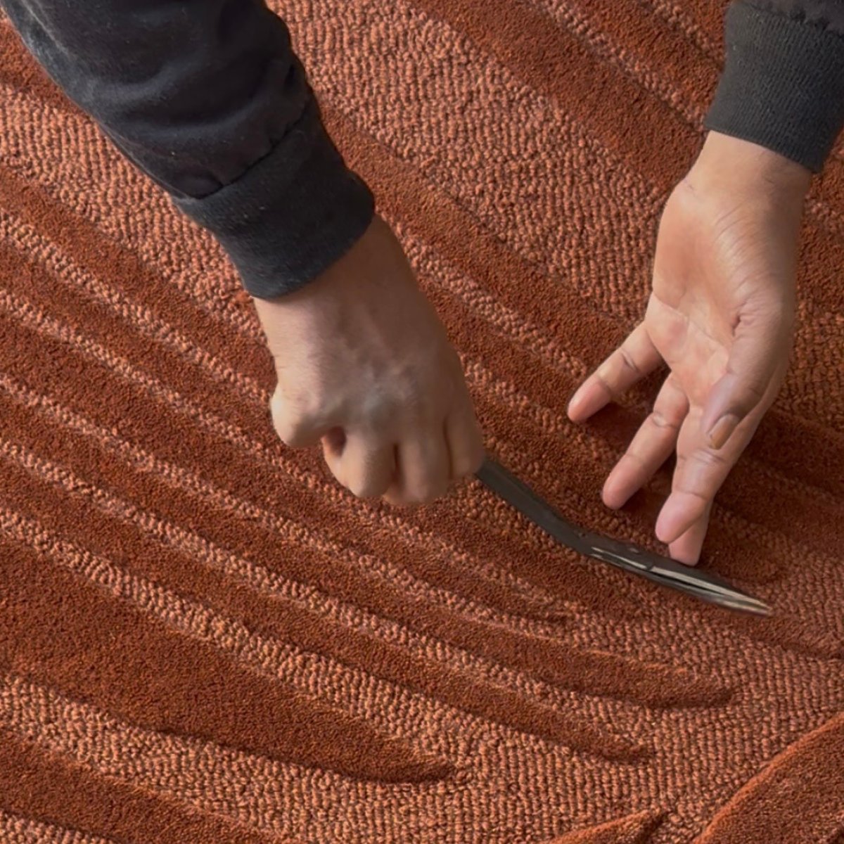 Artisan hand-carving the sculptural feather design into the Sway hand-tufted wool rug in rust by House of Bohi, using a traditional carving tool.