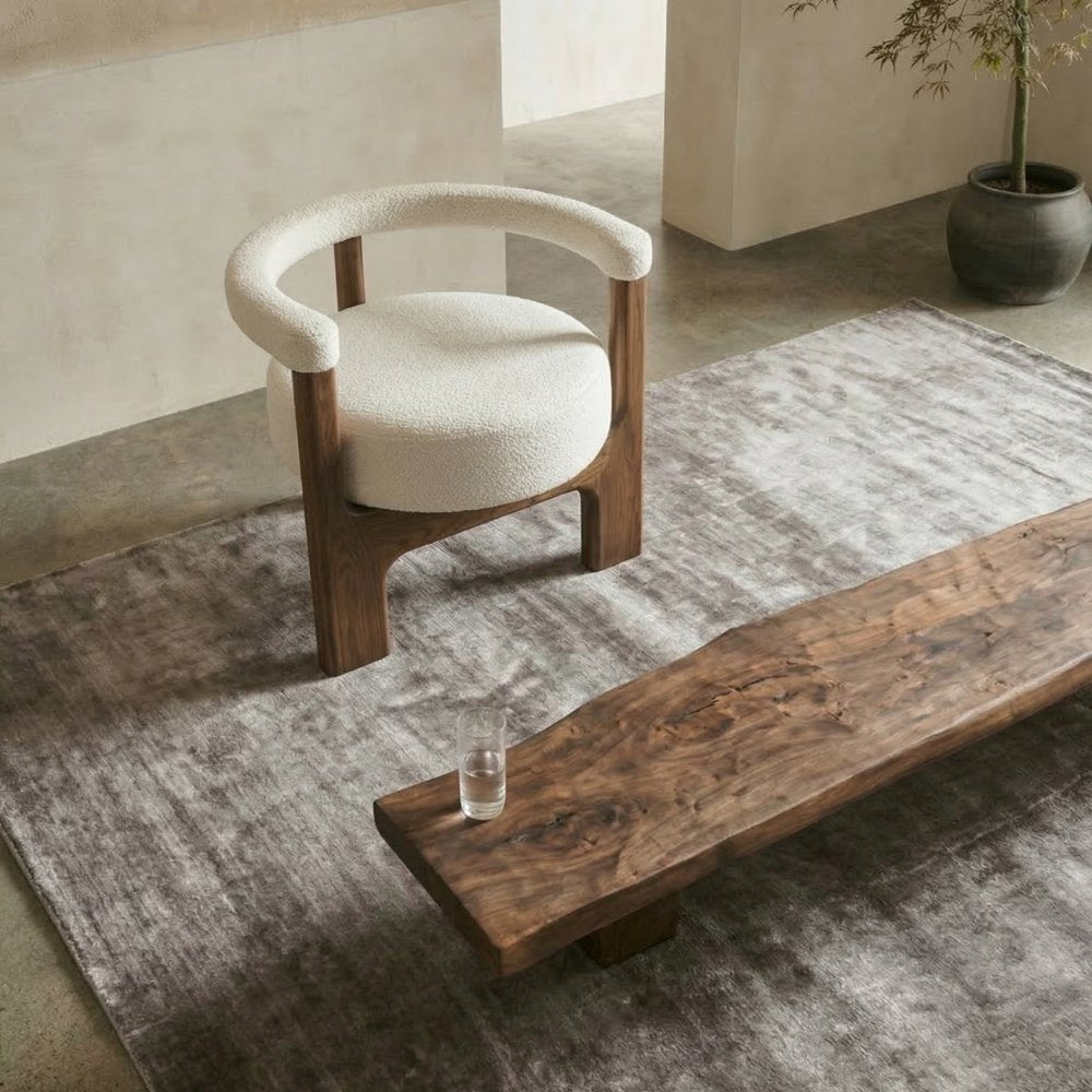 Handcrafted interior scene by House of Bohi featuring the Noor hand-loomed tencel rug in silver-grey, styled with a boucle armchair and a live-edge timber bench, reflecting the brand's slower, considered approach to rug-making.