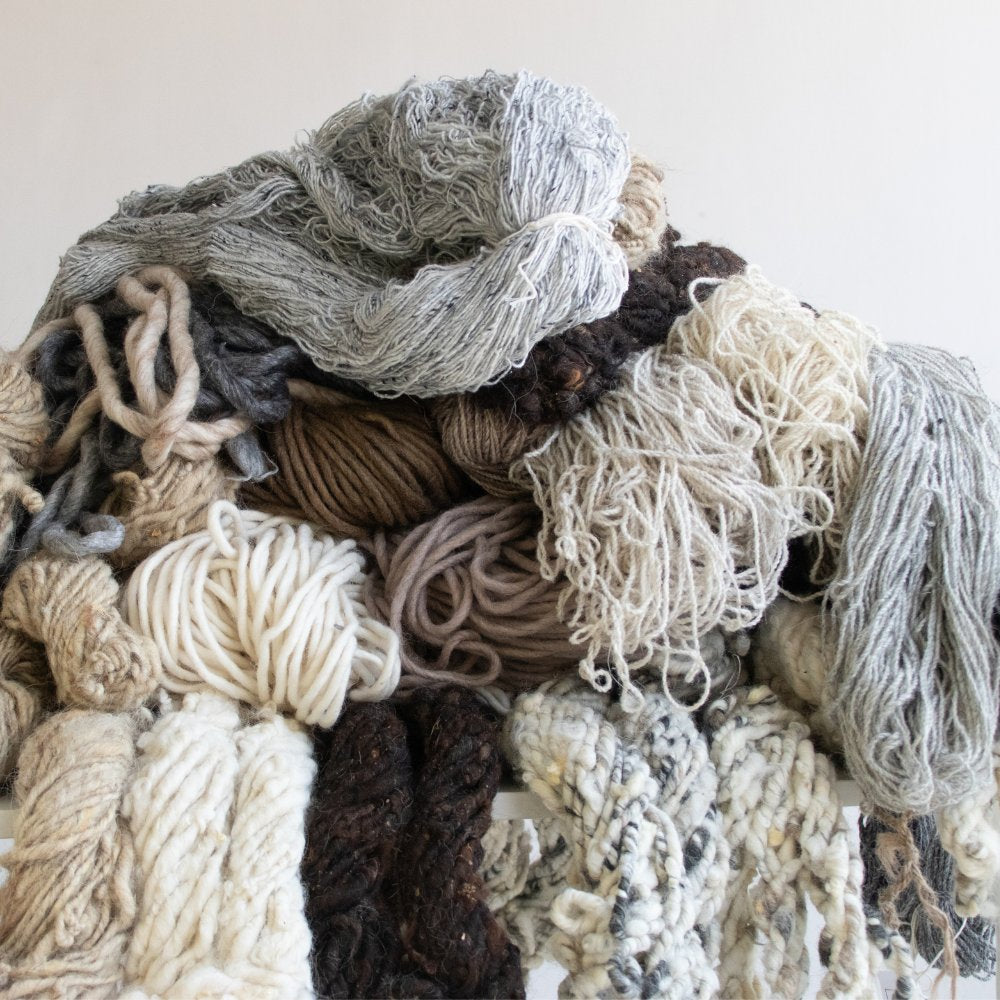 Stack of natural fibre yarns used in House of Bohi custom rugs, including wool, jute, tencel, silk, hemp and linen in ivory, stone, charcoal and brown tones.