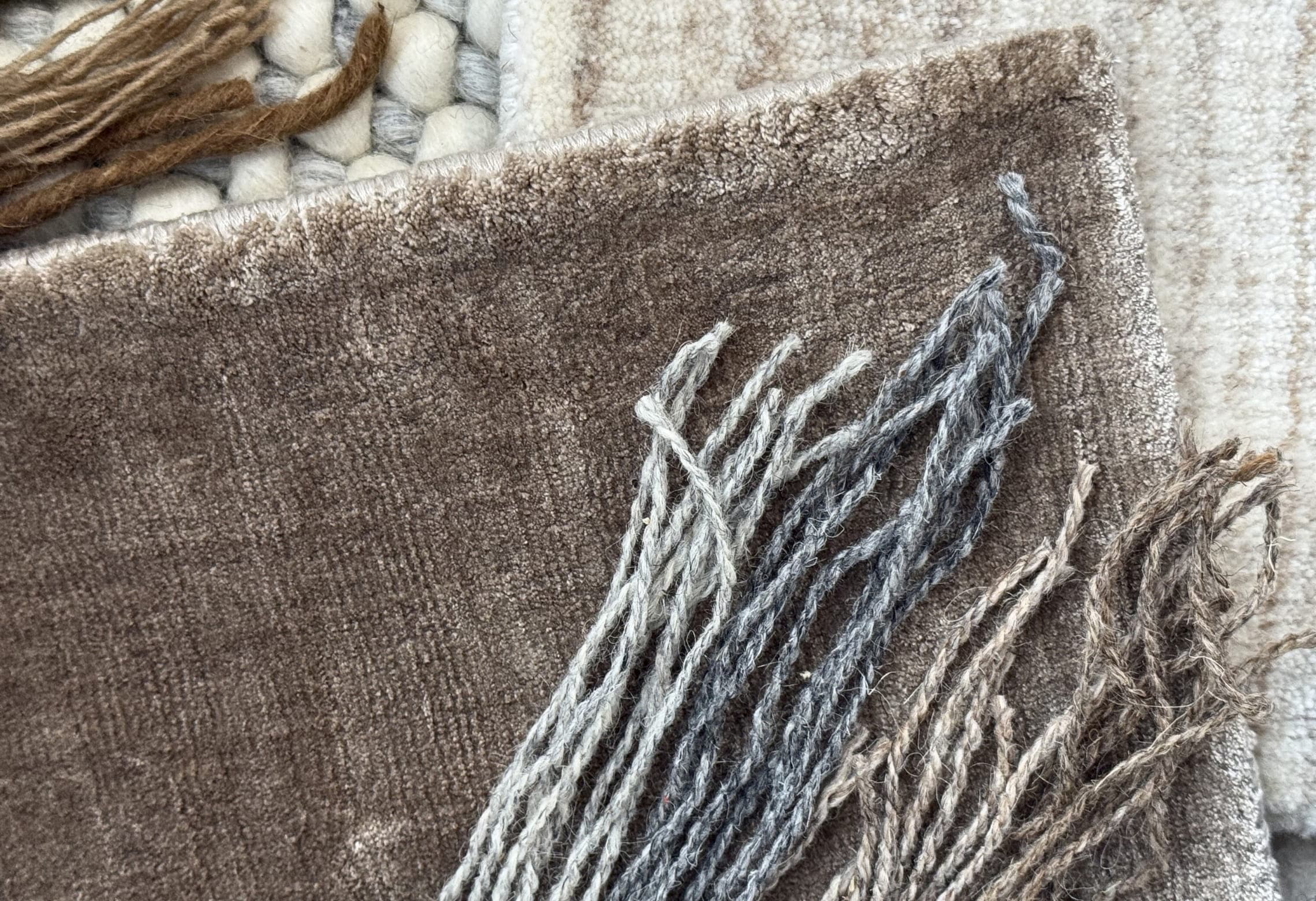 Layered sample of House of Bohi custom rugs, showing a hand-woven wool and jute flatweave alongside hand-loomed wool pile in brown, ivory and netural grey along with wool fibres placed on top.