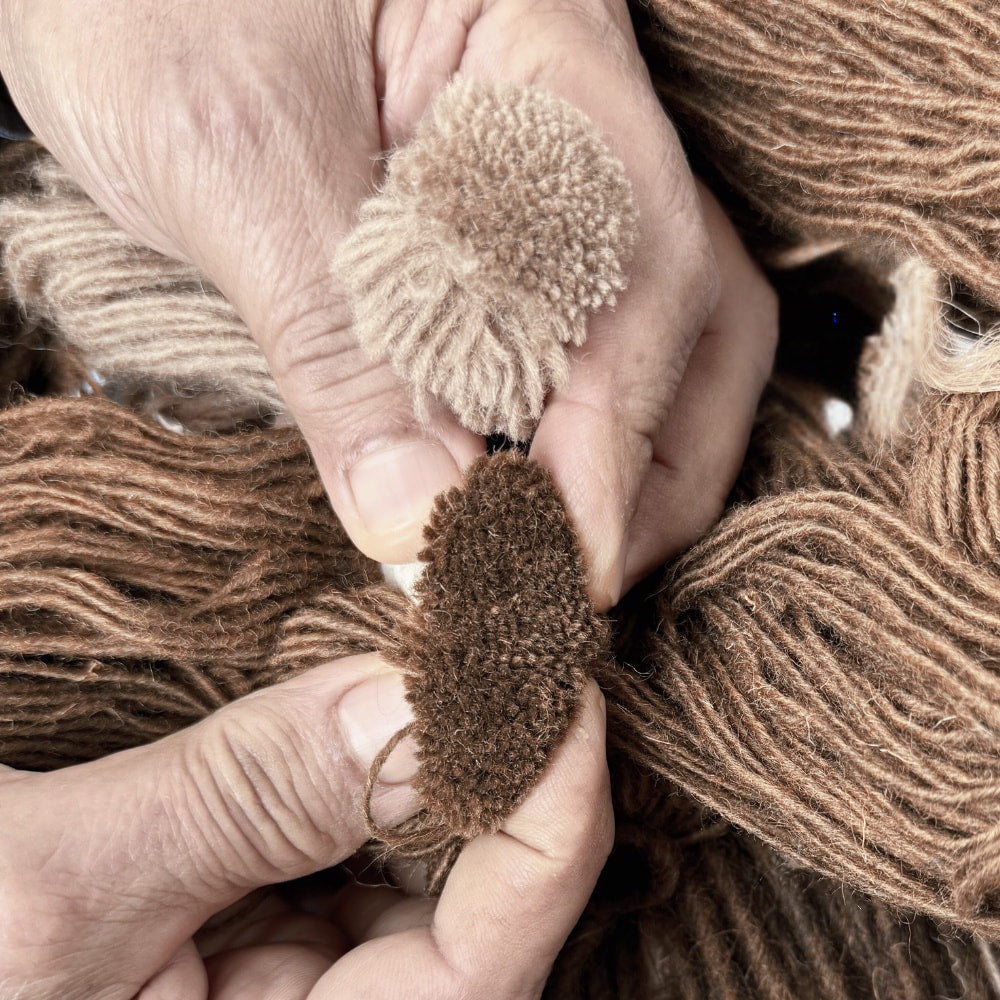 Sample-matching for a House of Bohi custom rug commission, comparing two hand-tufted wool pile samples in chocolate and camel against raw wool yarn to finalise the colourway.