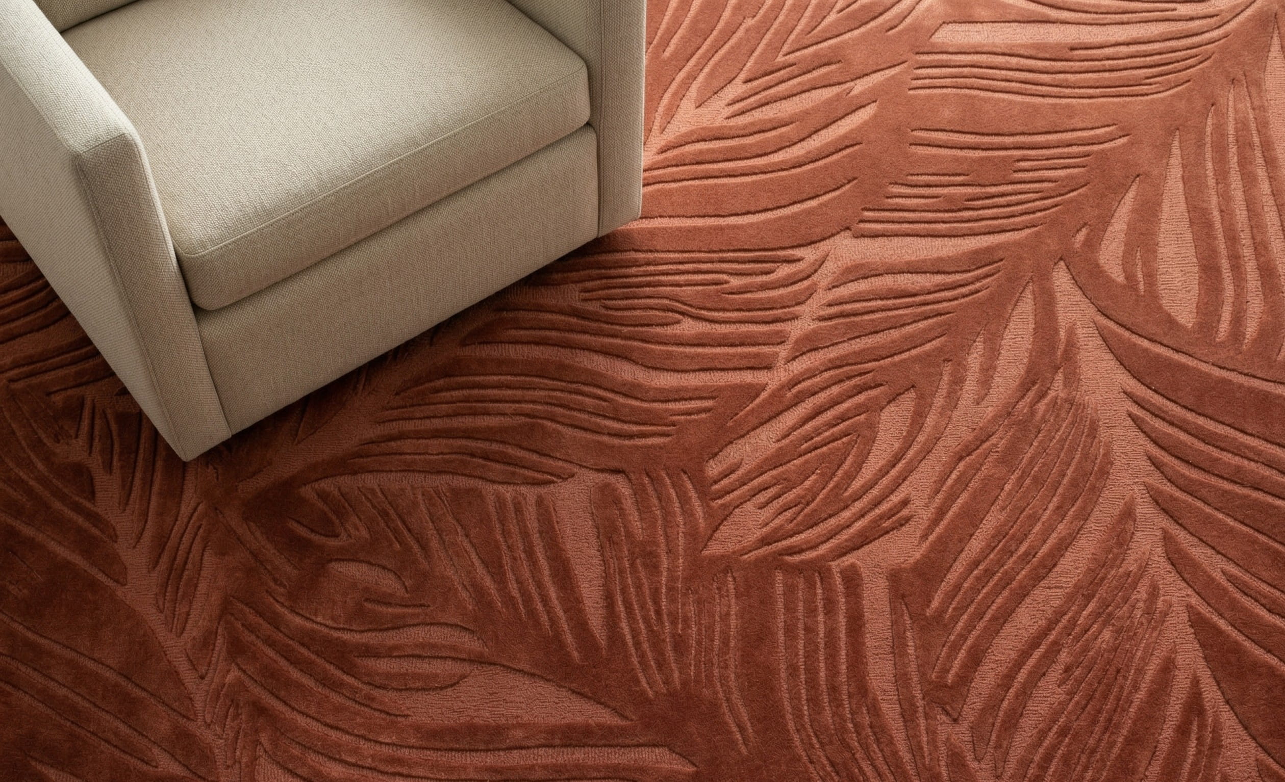 Sway hand-tufted New Zealand wool rug in rust by House of Bohi, with a sculptural carved leaf design and a cream linen armchair resting on top.