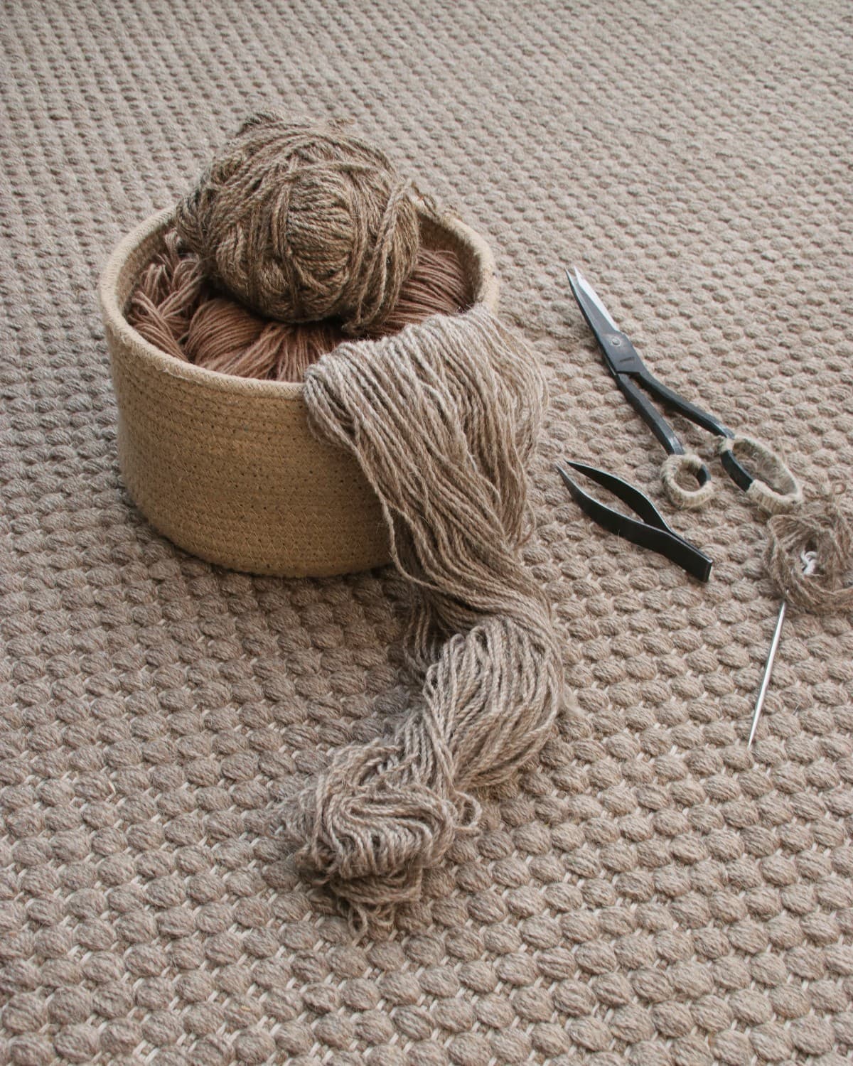 Basket of spun yarn and traditional weaving tools resting on the handmade rug, ethically crafted in Bhadohi, India.