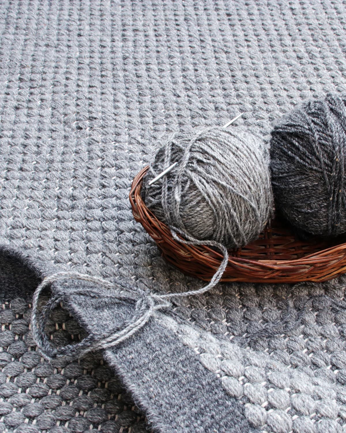 Woven basket holding spun yarn and traditional artisan tools resting on the handmade flatweave from Bhadohi, India.