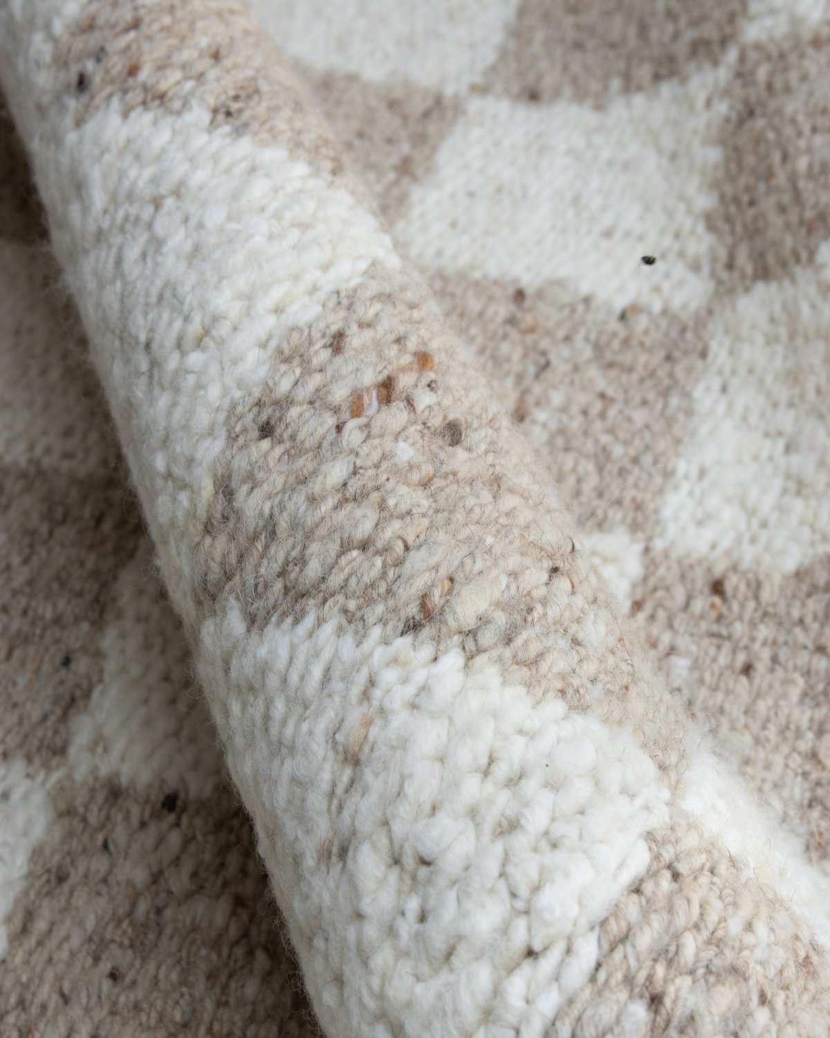 Folded drape showcasing the organic tonal variations and earthy presence of the handcarded wool in a 12mm pile height.