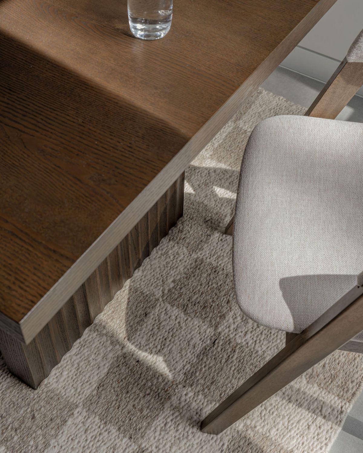 Overhead detail of Cora by House of Bohi, a plush undyed wool flatweave rug crafted from hand-carded wool, showing its natural cream and beige geometric pattern beneath a timber dining table and upholstered chair.