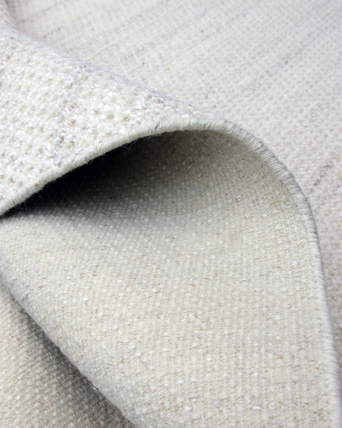 Folded corner revealing the handknotted edge of a minimalist wool rug, ethically crafted by GoodWeave artisans in Bhadohi.