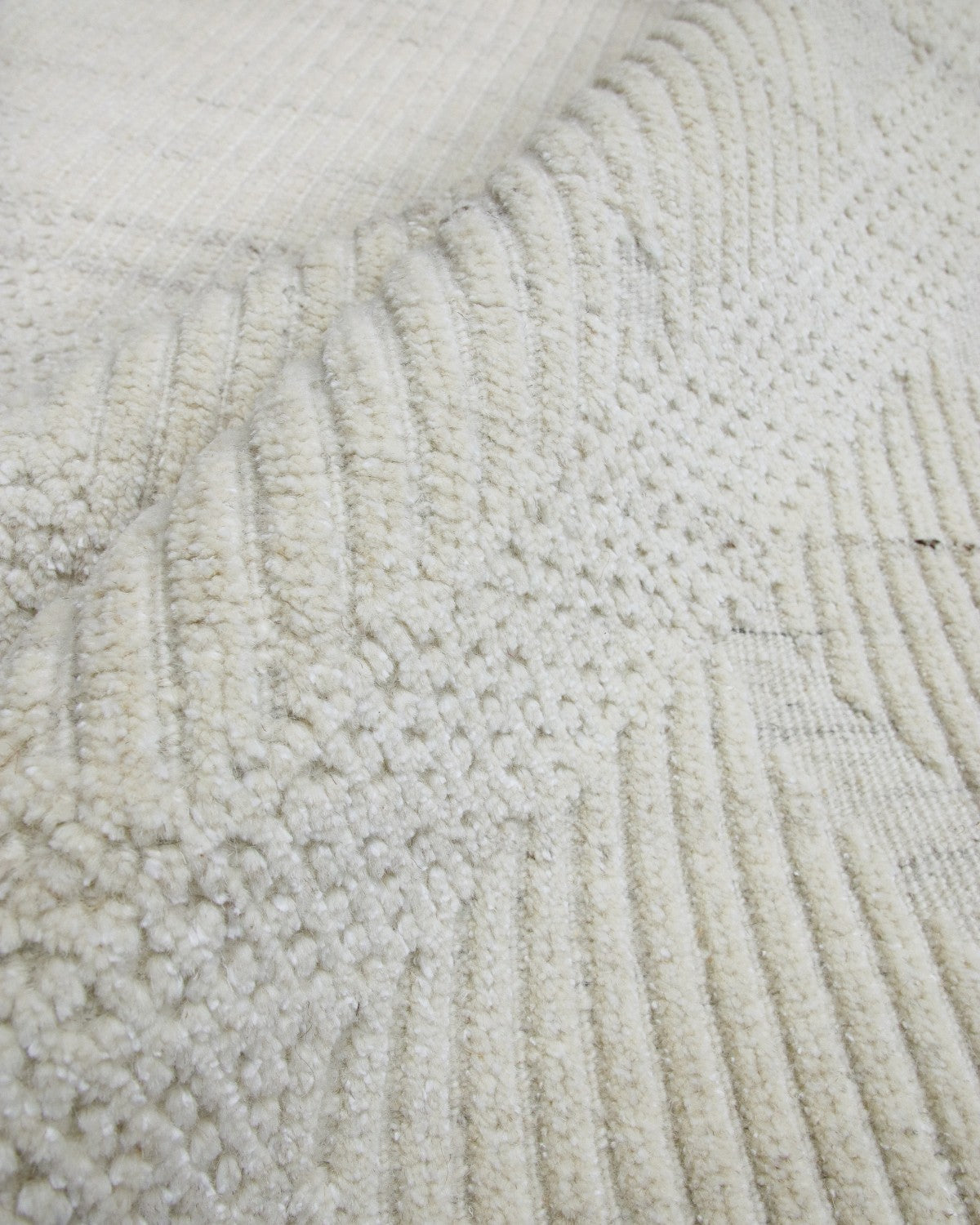 Macro texture of undyed handknotted wool, highlighting the 10mm pile height and modern relief classic diamond pattern.