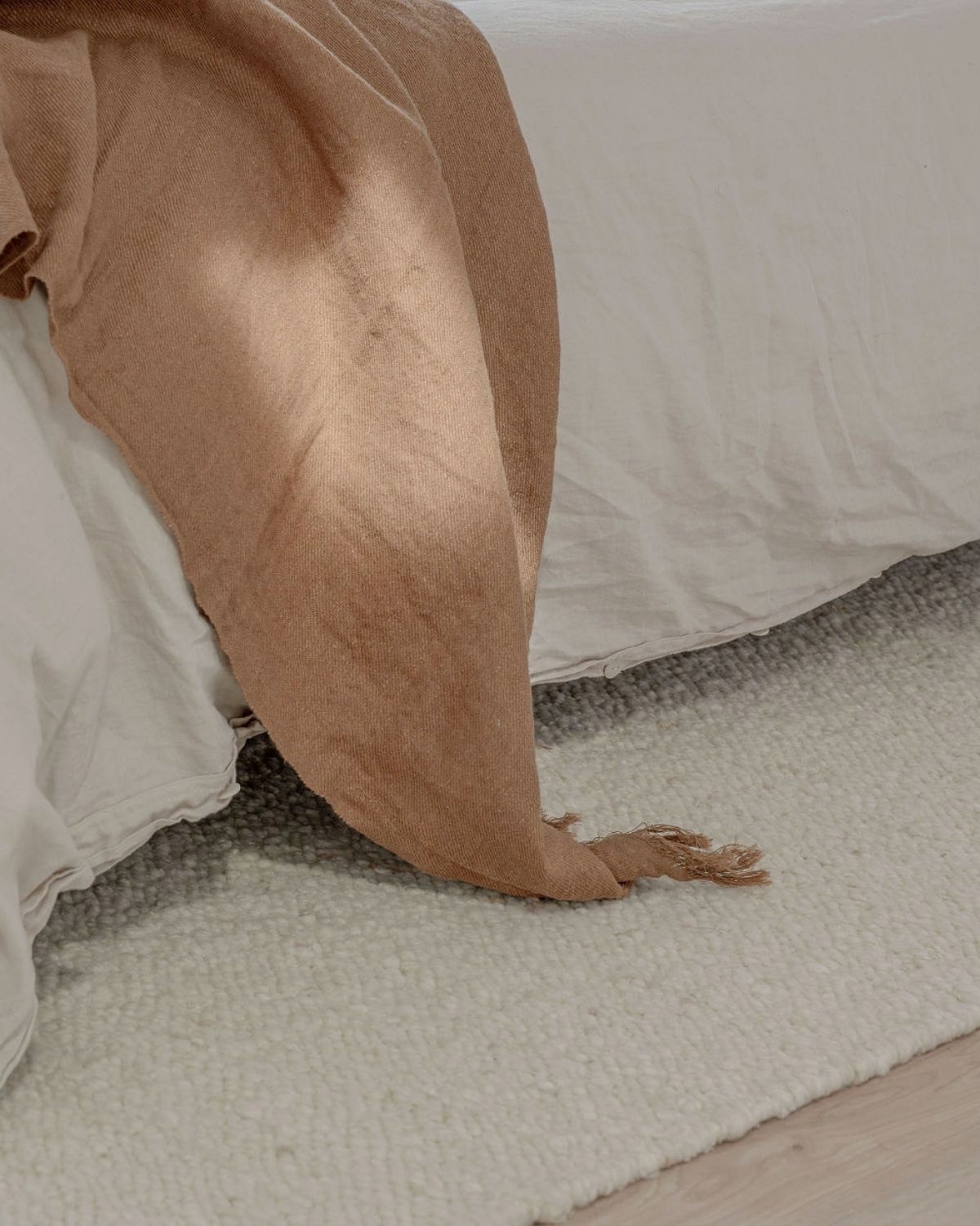 Mehi Ivory handwoven undyed wool rug by House of Bohi, styled in a contemporary bedroom with warm neutral bedding and a dark timber bedside table, featuring a soft, plush flatweave in natural ivory.