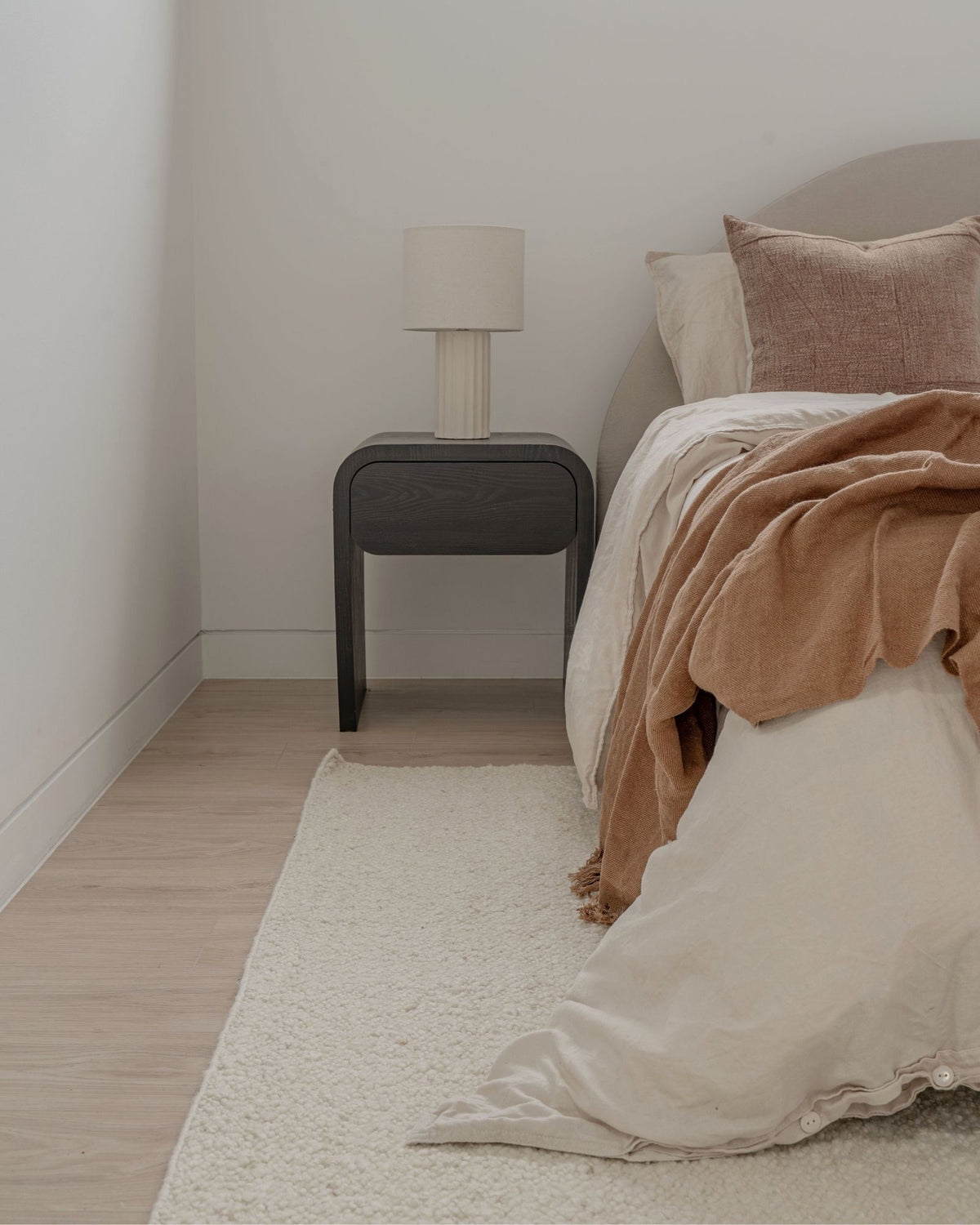 Mehi Ivory undyed wool rug by House of Bohi, styled beside a bed with soft terracotta linen, showcasing its plush hand-carded wool texture and natural ivory flatweave.