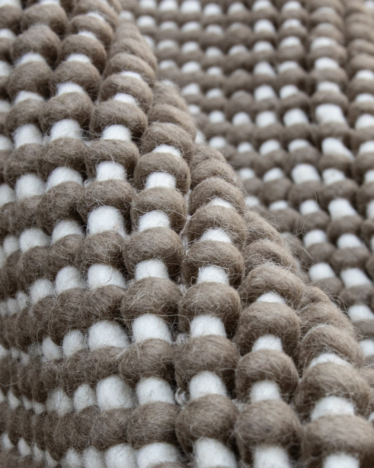 Close up of the chunky handwoven structure showing raised woollen knots inspired by the softened forms of river pebbles for unique plushness.