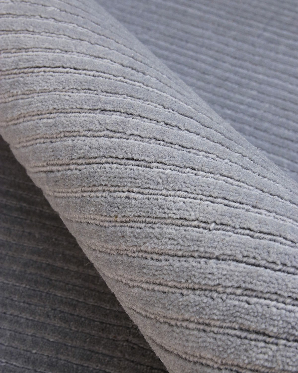 Macro detail of silver grey cut pile and fine loop-pile channels. A 12mm handloom weave for modern minimalist bedrooms.