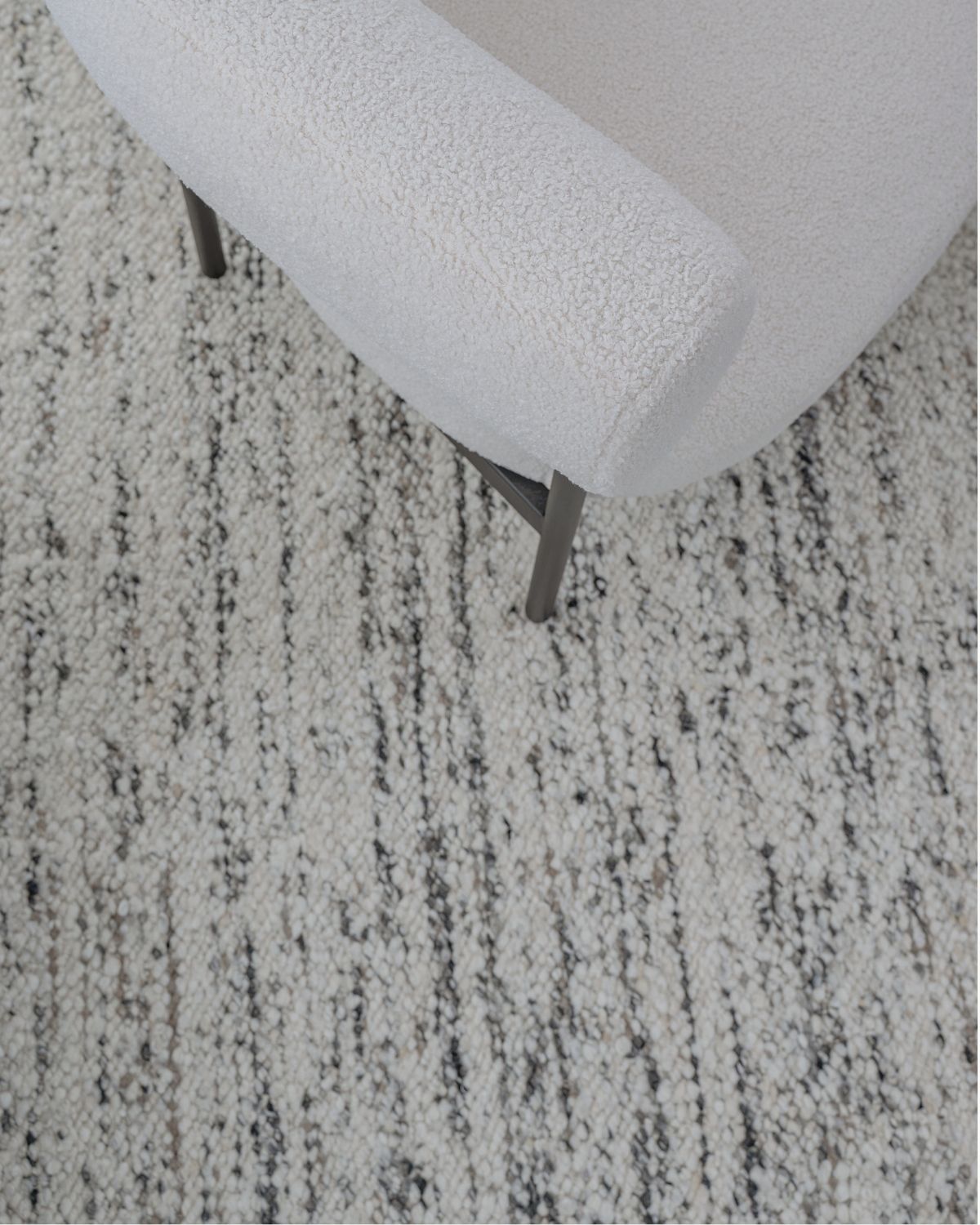 Close-up of Taalo Ashstone undyed wool rug by House of Bohi, styled beneath a sculptural cream armchair, highlighting its plush hand-carded wool flatweave and natural ivory, ash grey and charcoal fibres.