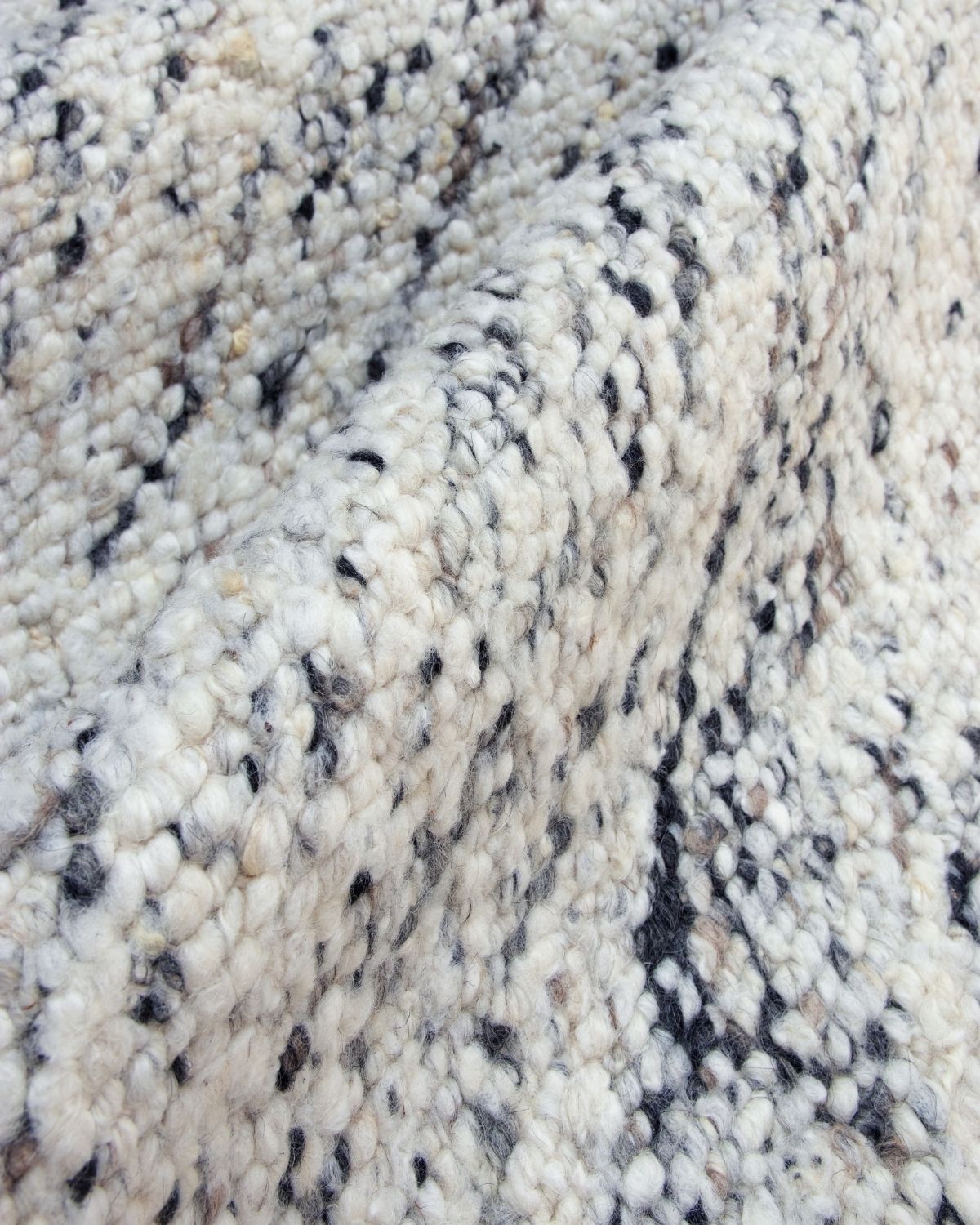 Macro close-up of Taalo Ashstone by House of Bohi, a handwoven, dye-free, undyed wool rug featuring plush hand-carded wool, chunky flatweave texture and natural ivory, ash grey, charcoal and brown fibres.