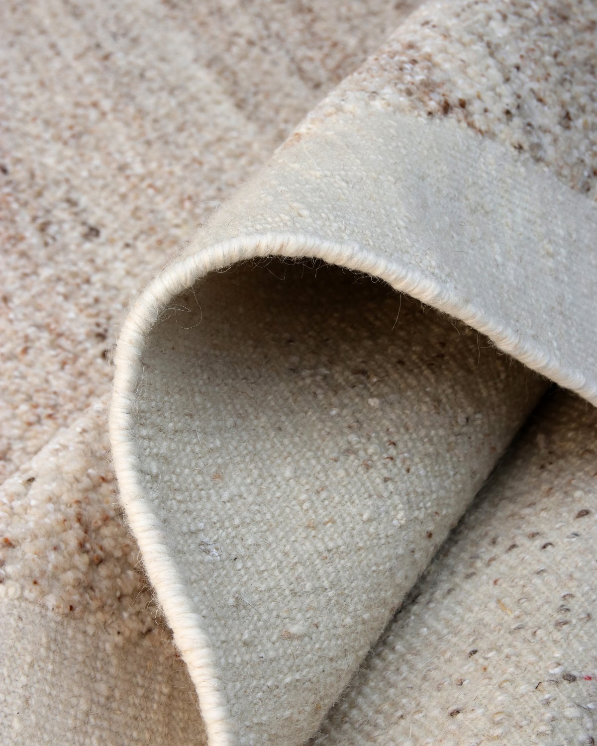 Corner of Akira hand-knotted wool rug in Dune, showing the flat woven ivory border framing the striated beige and brown pile
