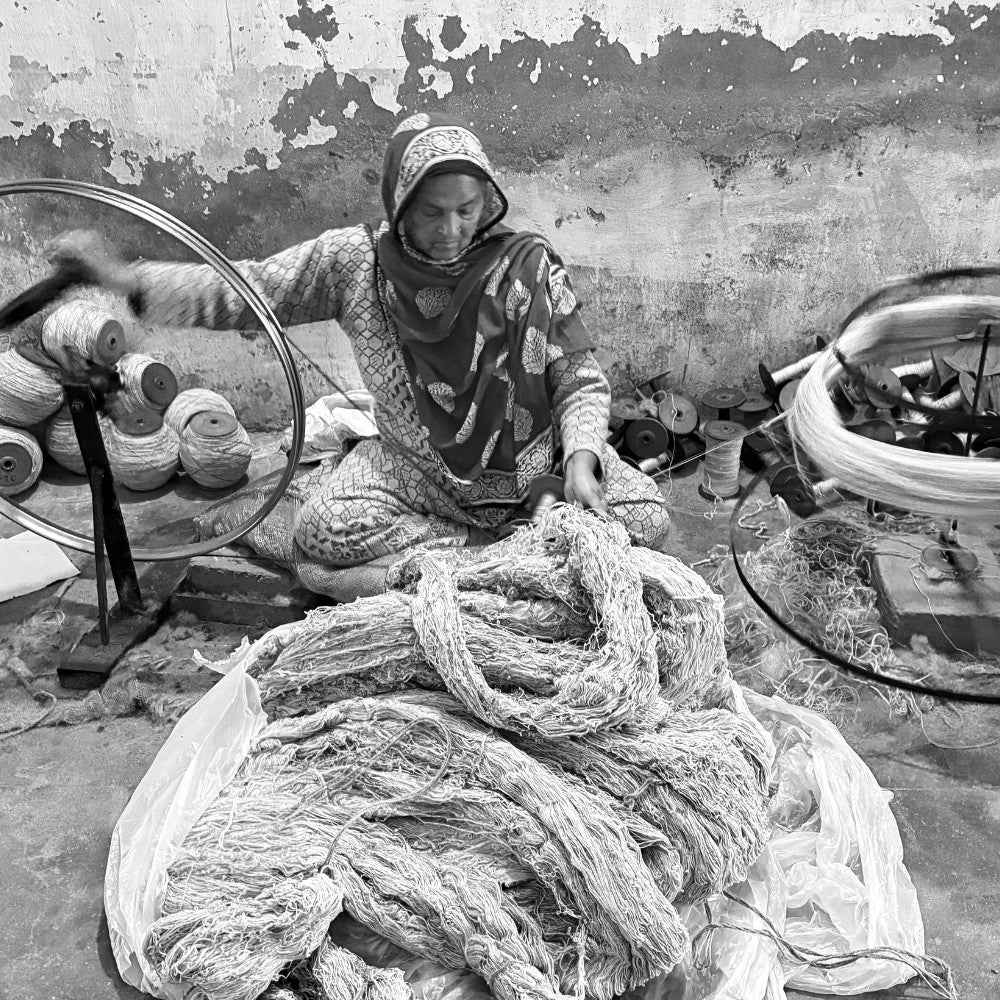 Black and white photograph of a woman artisan hand-spinning yarn on a traditional spinning wheel for House of Bohi, working within the family-led weaving community in Bhadohi, India.