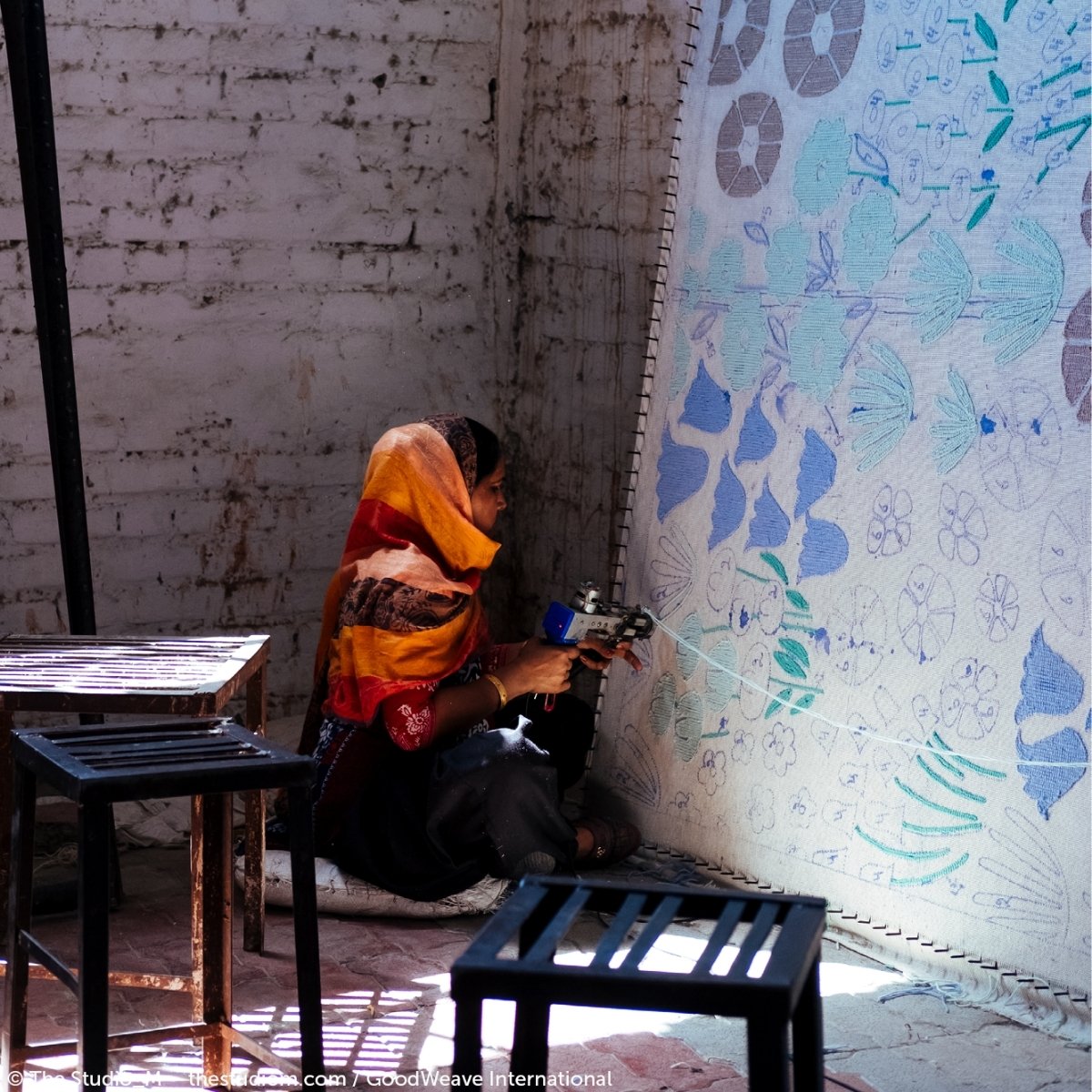 An artisan woman hand tufting a wool rug in India in an official GoodWeave photograph.
