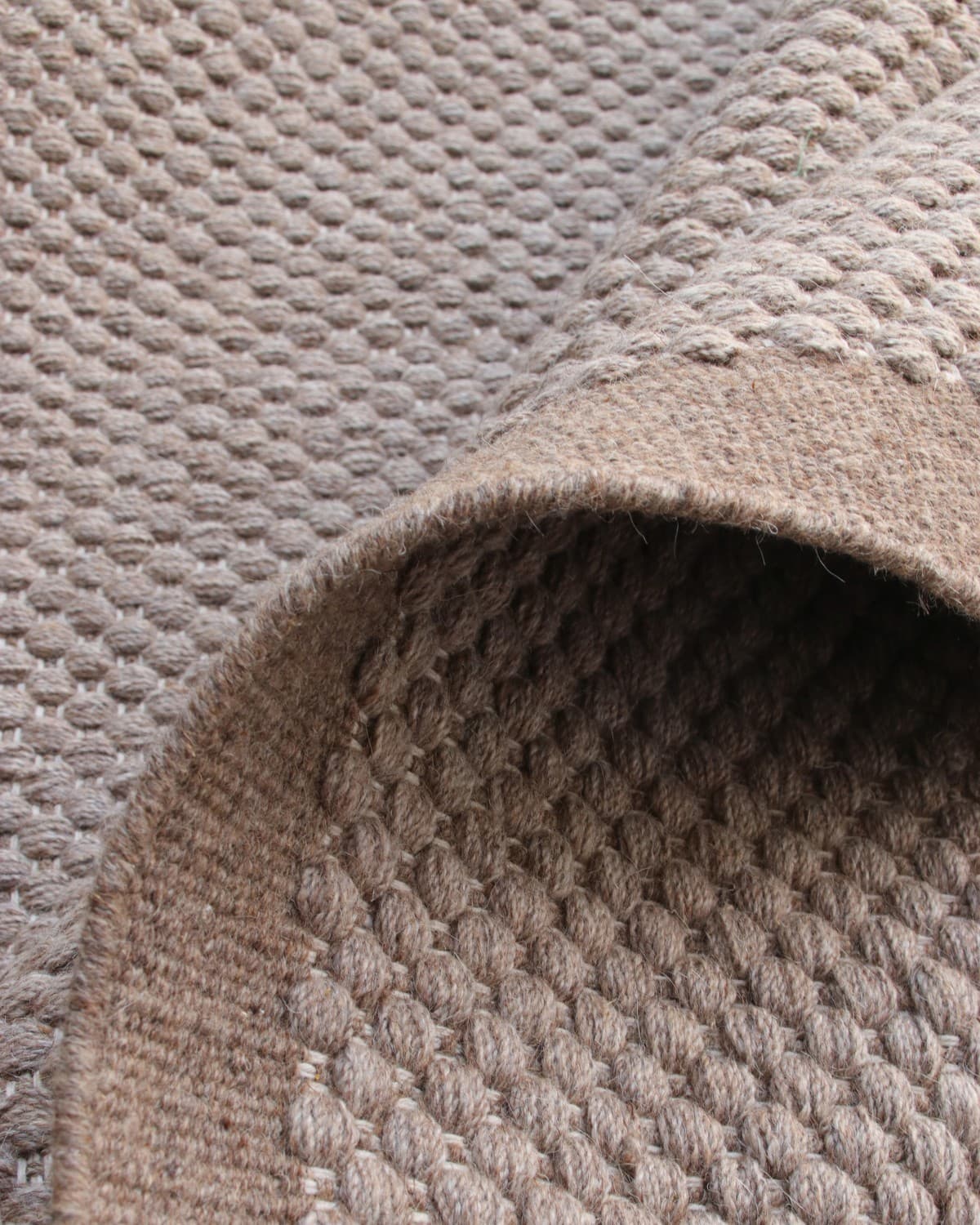 Folded edge detailing the smooth transition from a beaded wool body to a clean, artisan-finished solid border.