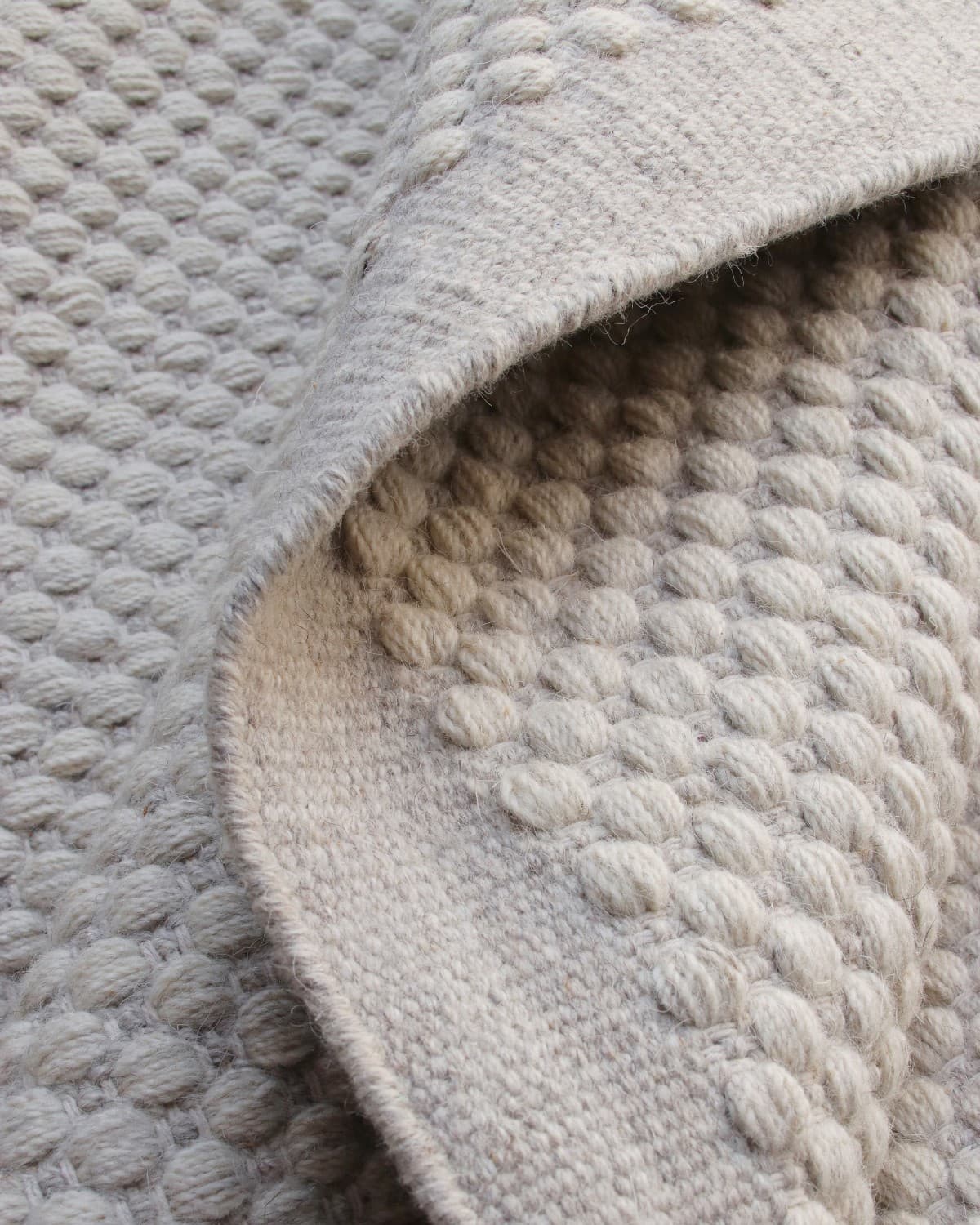 Folded edge detailing the transition from a beaded wool center to a seamless flatweave border for a modern study.