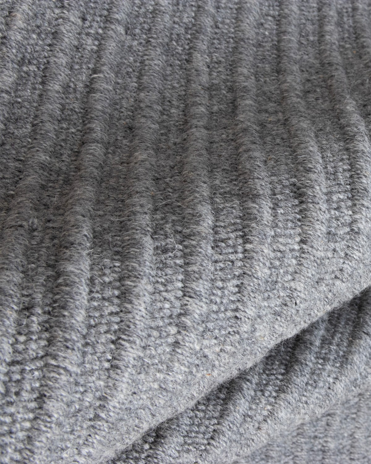 Draped reversible flatweave revealing subtle tactile relief and a 12mm pile height, ideal for a structured living room.