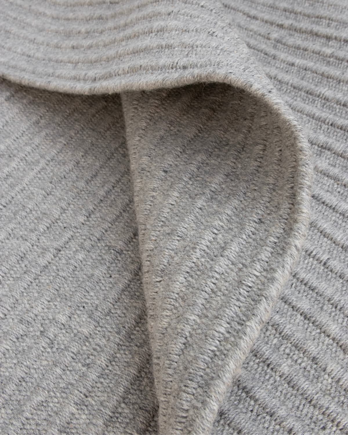 Folded reversible grey rug highlighting a quiet linear form, ethically handmade in Bhadohi, India for a living room.