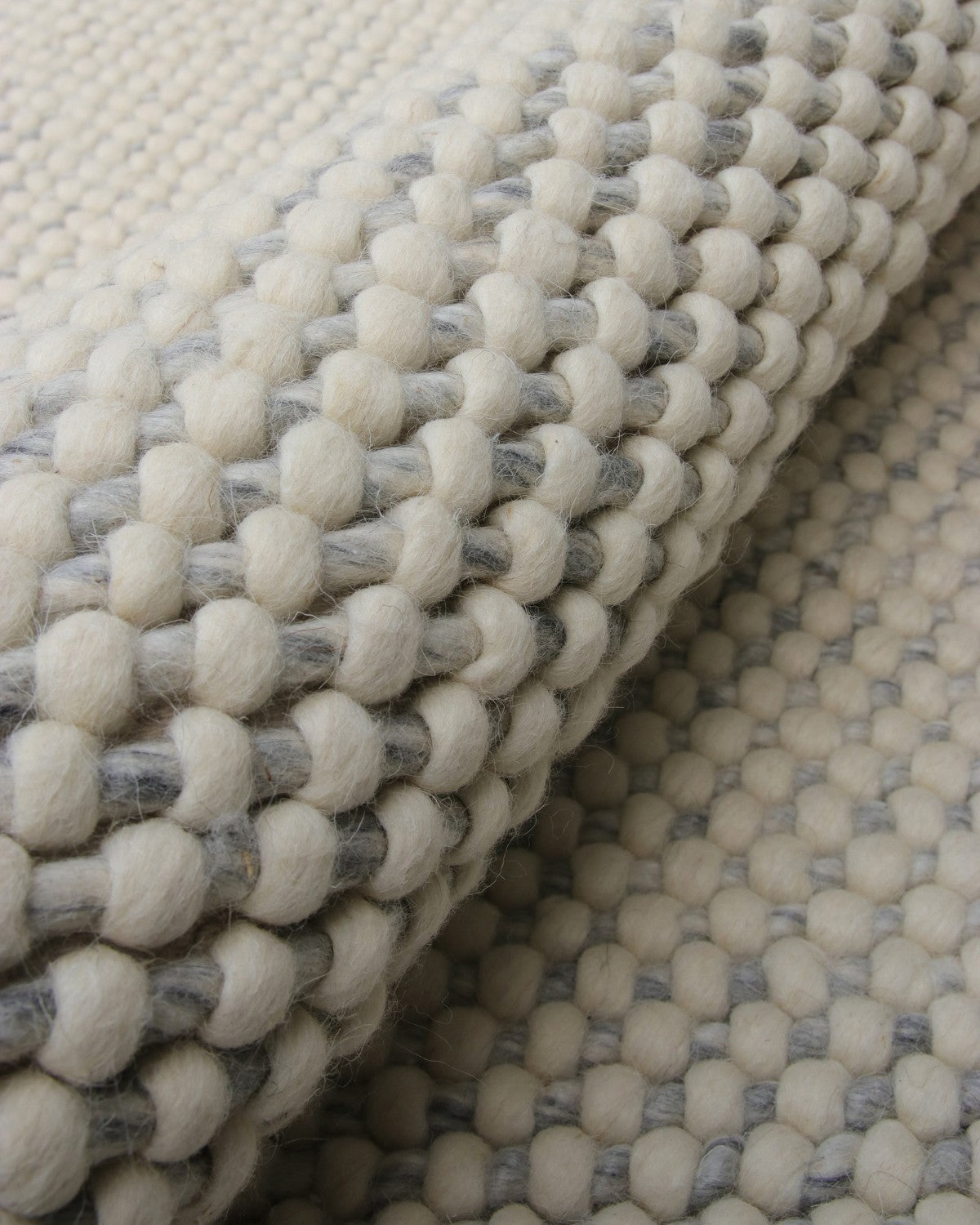 Close up of the chunky handwoven structure showing raised woollen knots inspired by river pebbles for unique plushness.