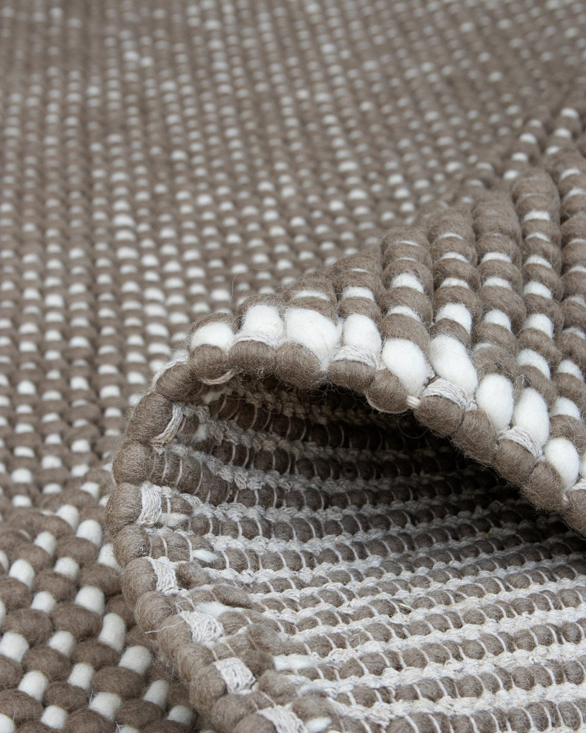 A folded corner reveals the resilient handwoven flatweave and 20mm pile, grounding a bedroom or living room with earthy texture and quiet comfort.
