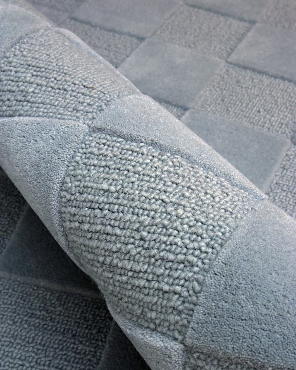 A rolled section reveals meticulous craftsmanship, displaying the rich 15mm pile height and tight hand-tufted loop weave.