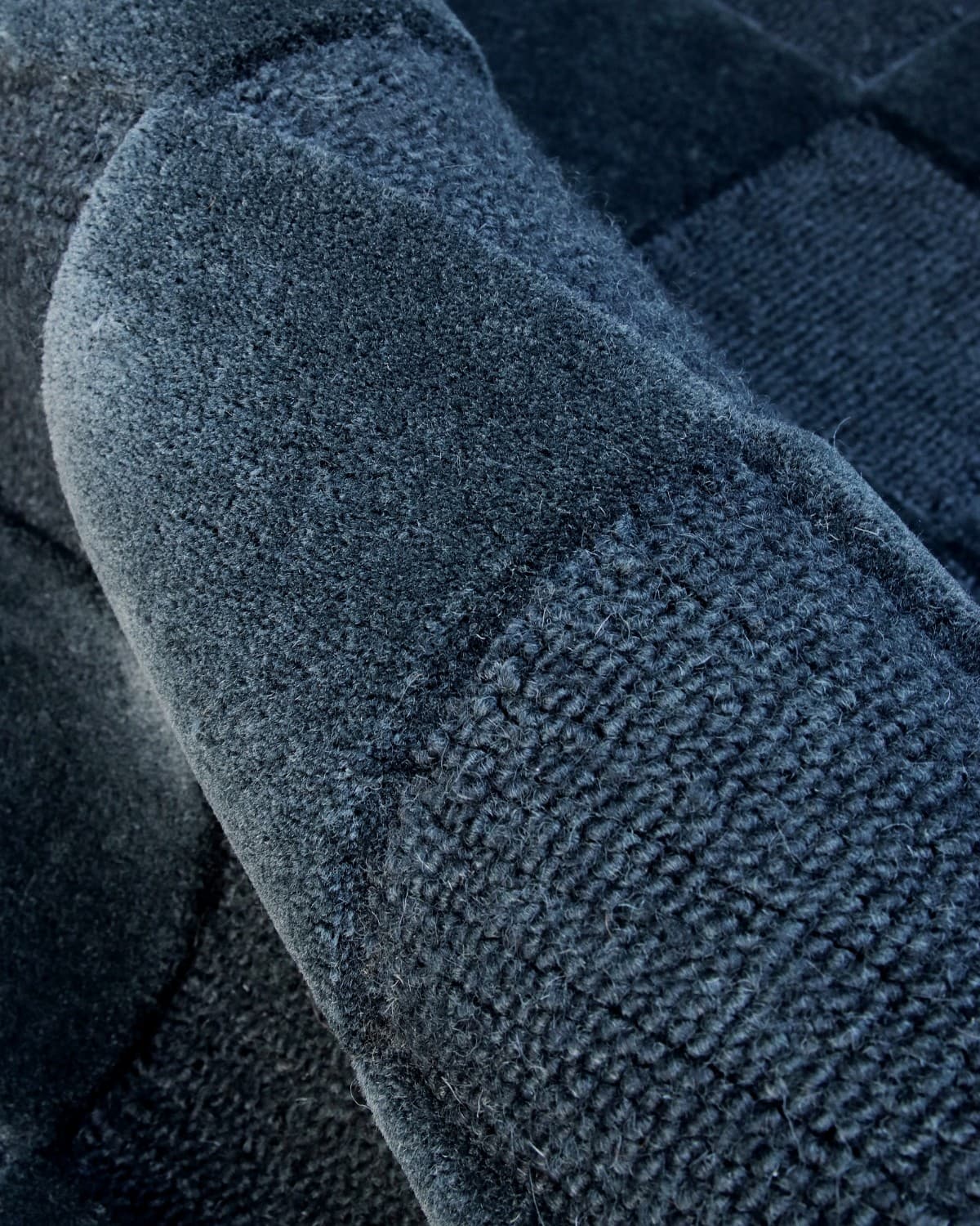 A rolled close-up highlights the meticulous craftsmanship, rich 15mm pile height, and tight hand-tufted loop weave.