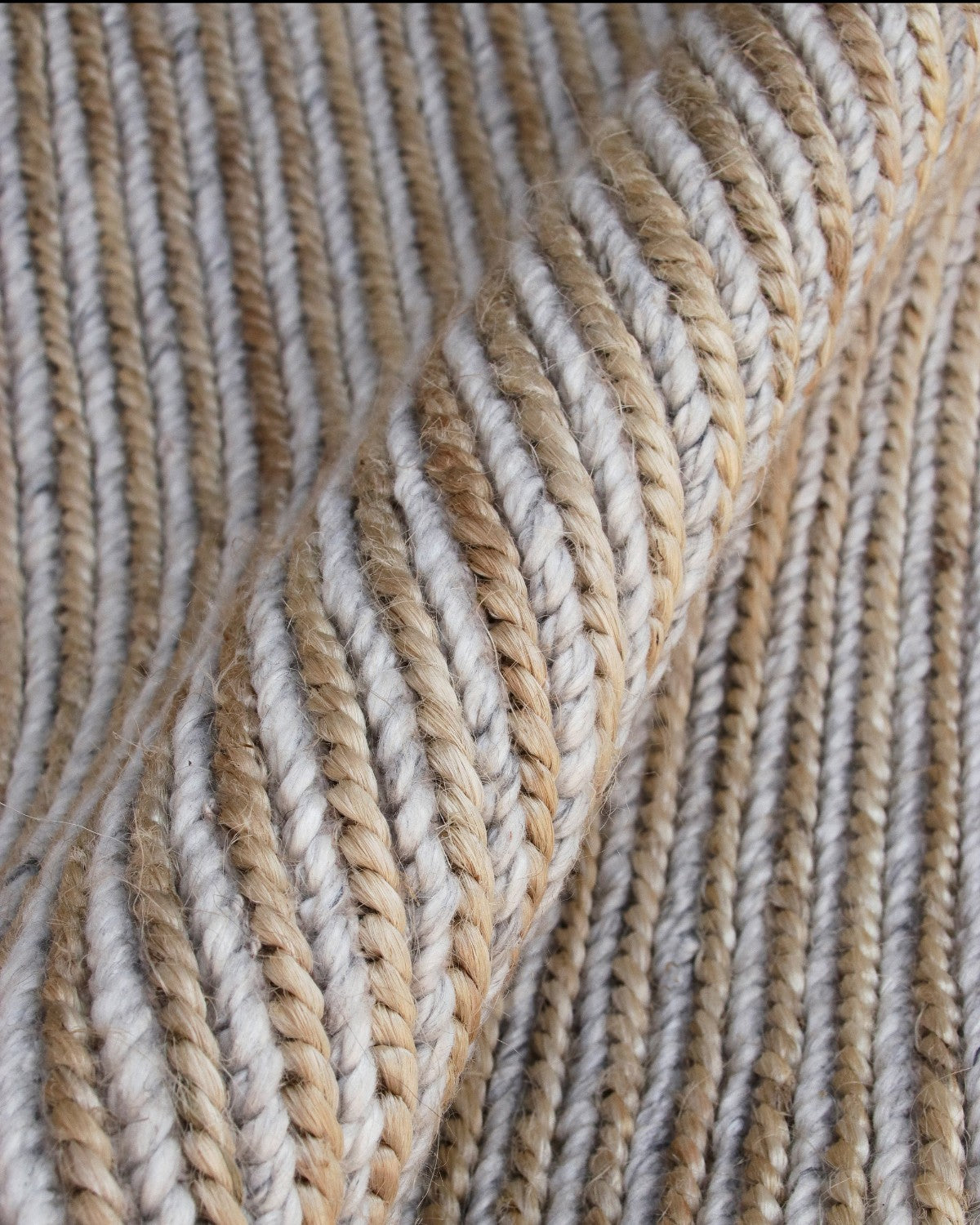 Close up of thick, twisted cords intertwining soft wool with robust natural jute to form a rhythmic, braid-like texture.