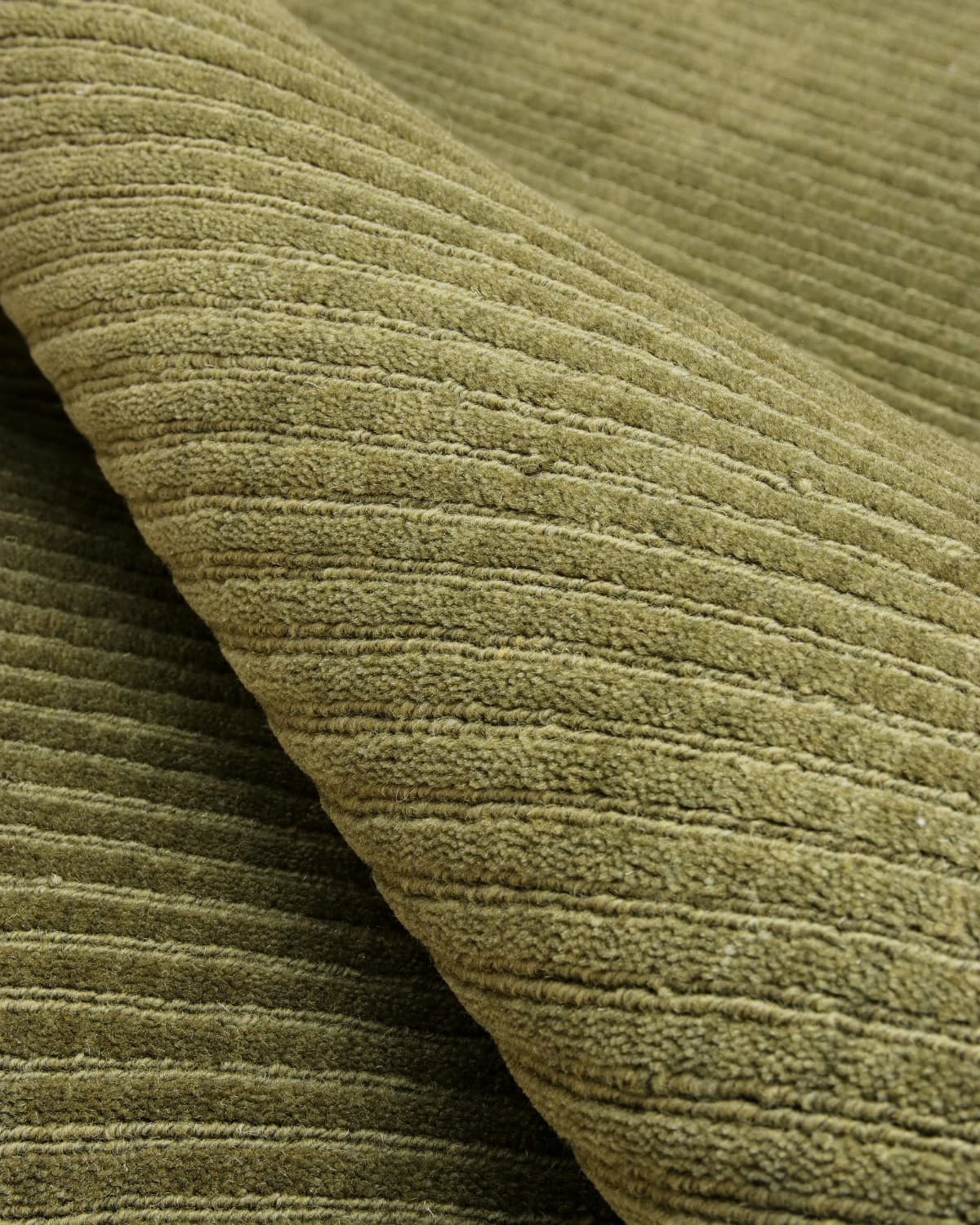 Macro detail of olive cut pile and fine loop-pile channels. A plush 12mm handloom weave ideal for modern minimalism.