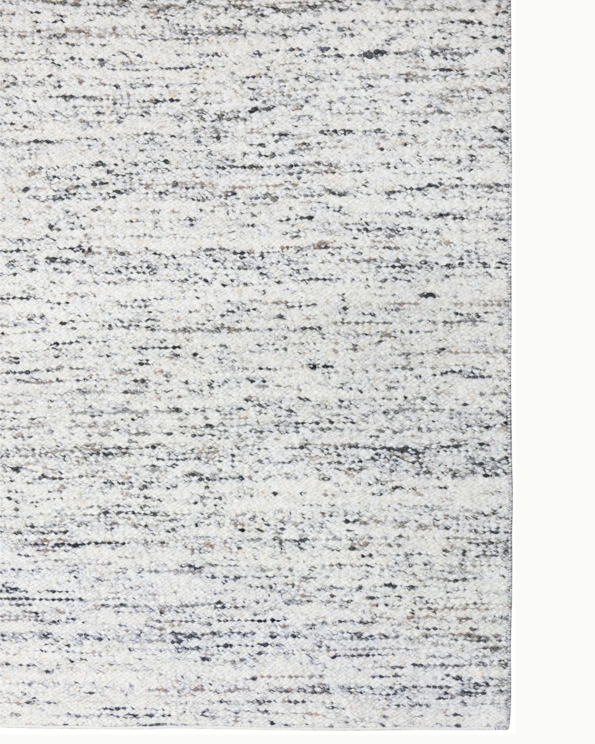 Close-up detail of Taalo Ashstone, a handwoven undyed wool rug featuring plush hand-carded wool, natural ash grey and charcoal tones with subtle earthy brown flecks and a richly textured flatweave.