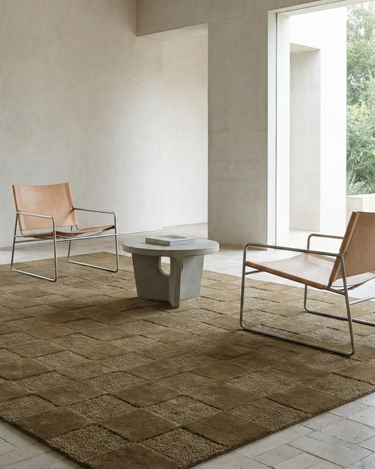 Navo hand-tufted wool rug in loden green by House of Bohi, featuring a tonal checkerboard design, styled with tan leather chairs and a stone side table.