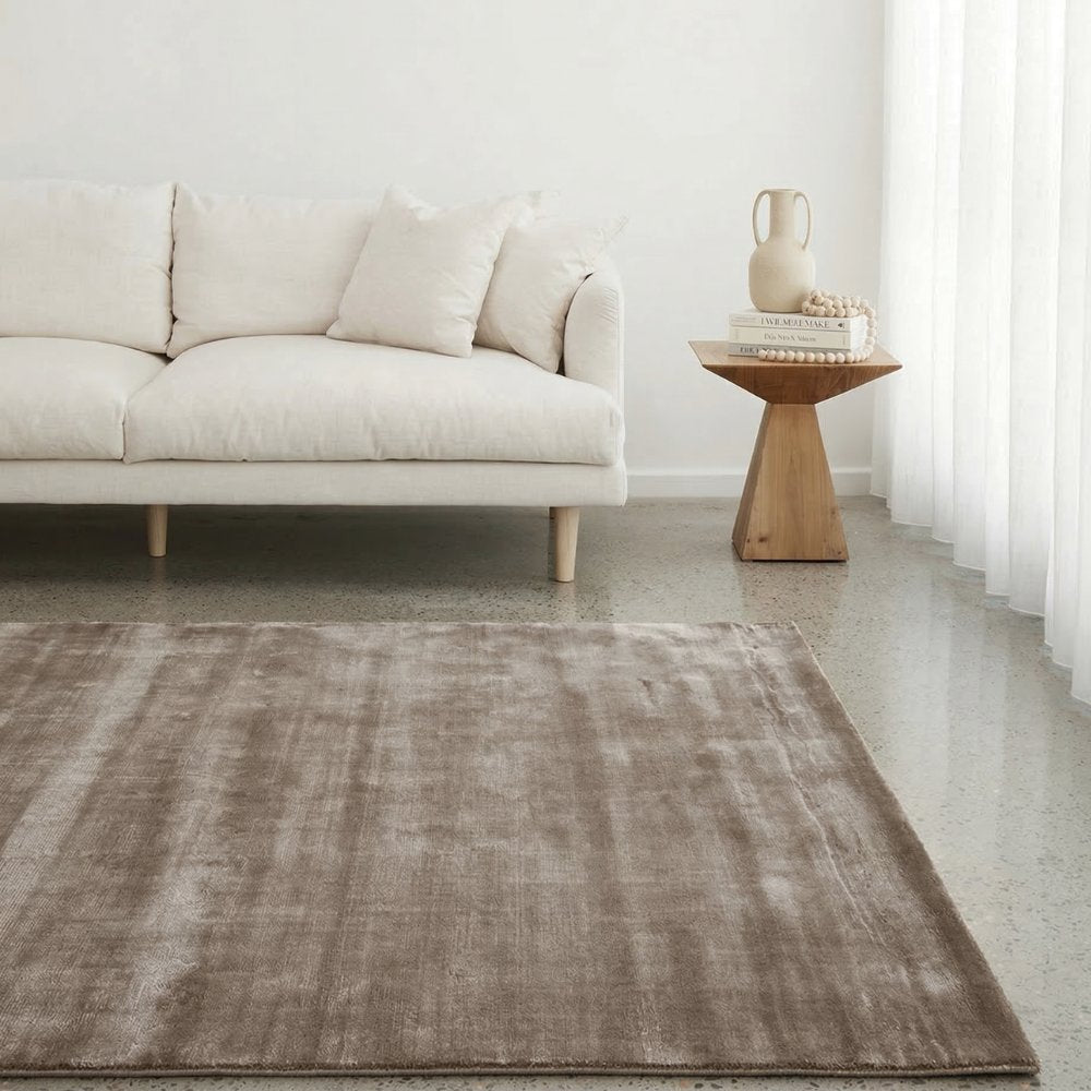 Noor hand-loomed tencel rug in warm taupe by House of Bohi, styled in a minimalist living room with a cream linen sofa, timber side table and sheer linen curtains.