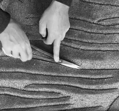A weaver hand-shears and carves the surface of a handwoven rug to refine its texture and definition at the House of Bohi workshop in Bhadohi, India.