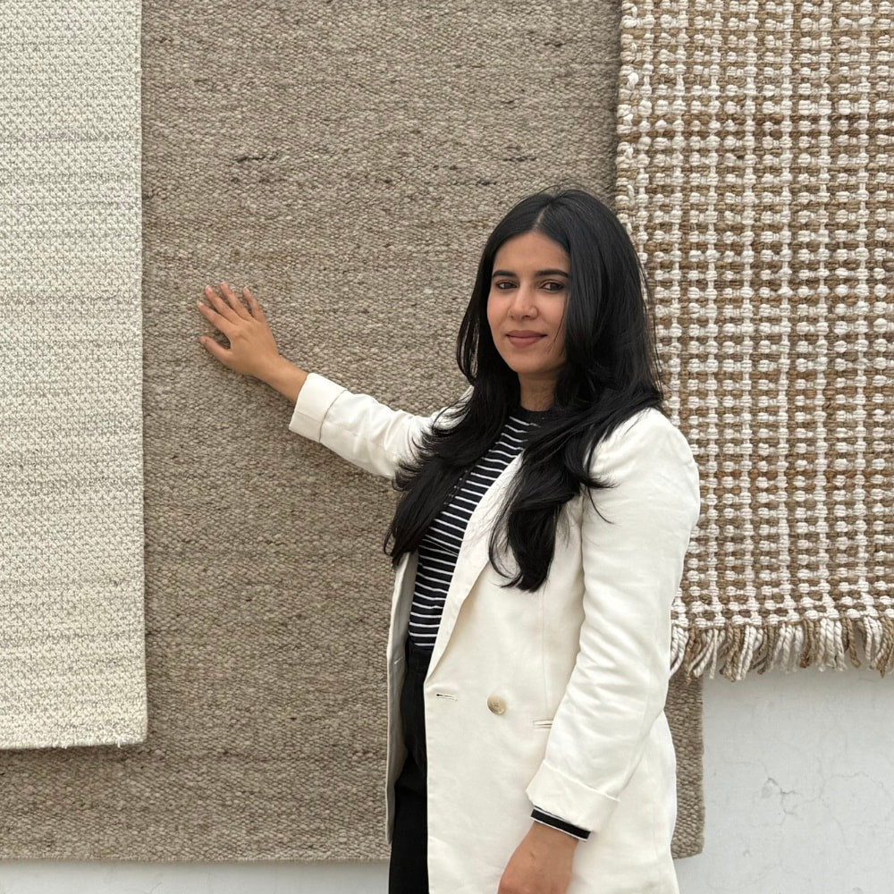 Saima Abrar, founder of House of Bohi, photographed with a collection of handwoven wool and jute rugs from her family's four-generation rug-making lineage in Bhadohi, India.
